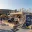 Foto Ein moderner, zweistöckiger Event-Pavillon aus hellem Holz und Stahl auf einem belebten Stadionvorplatz. Das Modul verfügt über eine untere Verkaufsfläche mit Sitzgelegenheiten und eine obere Terrasse mit Fahrrädern und Logo-Bannern der Marke „Ascend“.