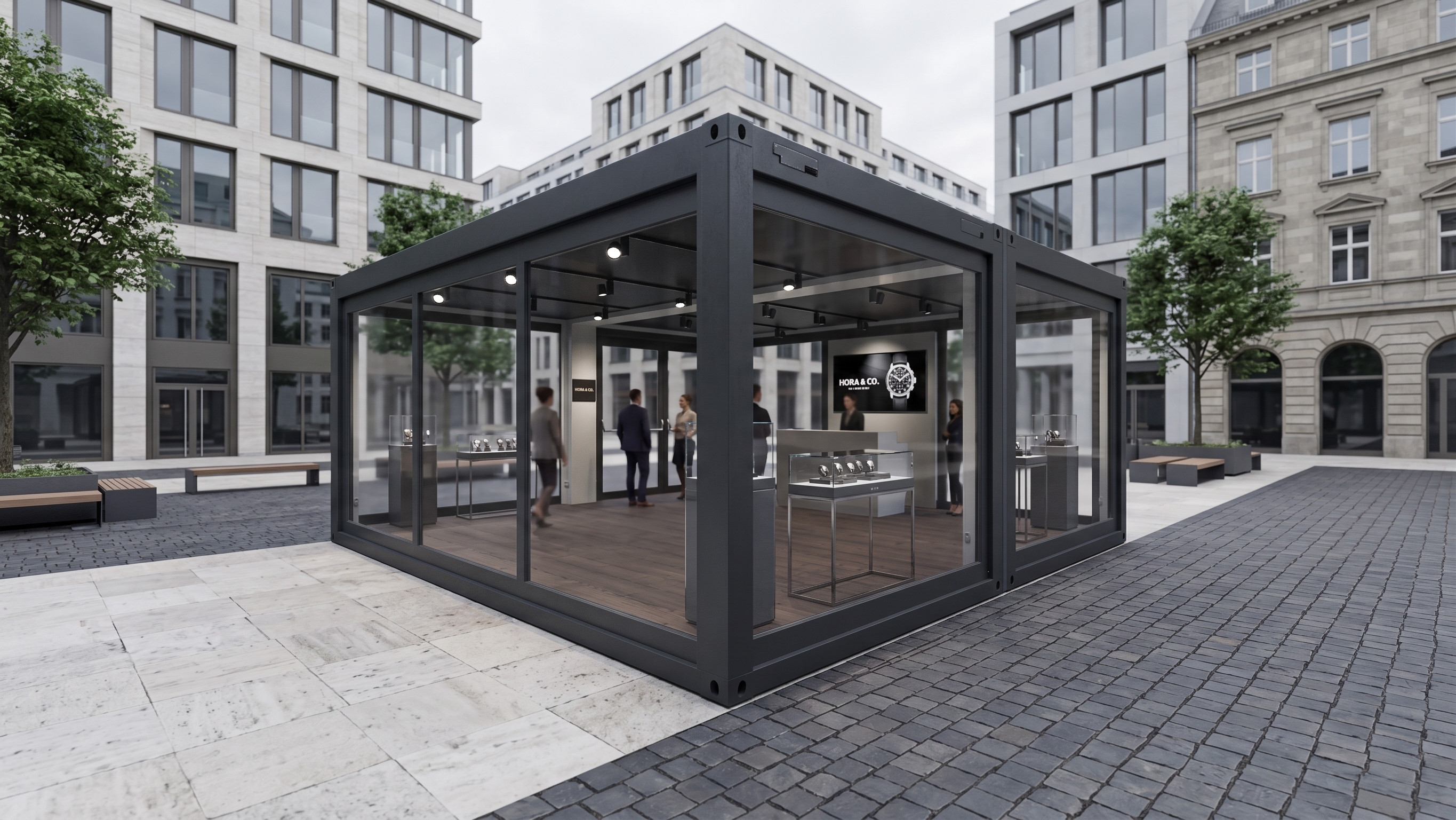 Außenansicht eines modernen, schwarz gerahmten Glascontainers (Showroom) auf einem gepflasterten Stadtplatz, in dem Uhren und Schmuck in Vitrinen präsentiert werden.